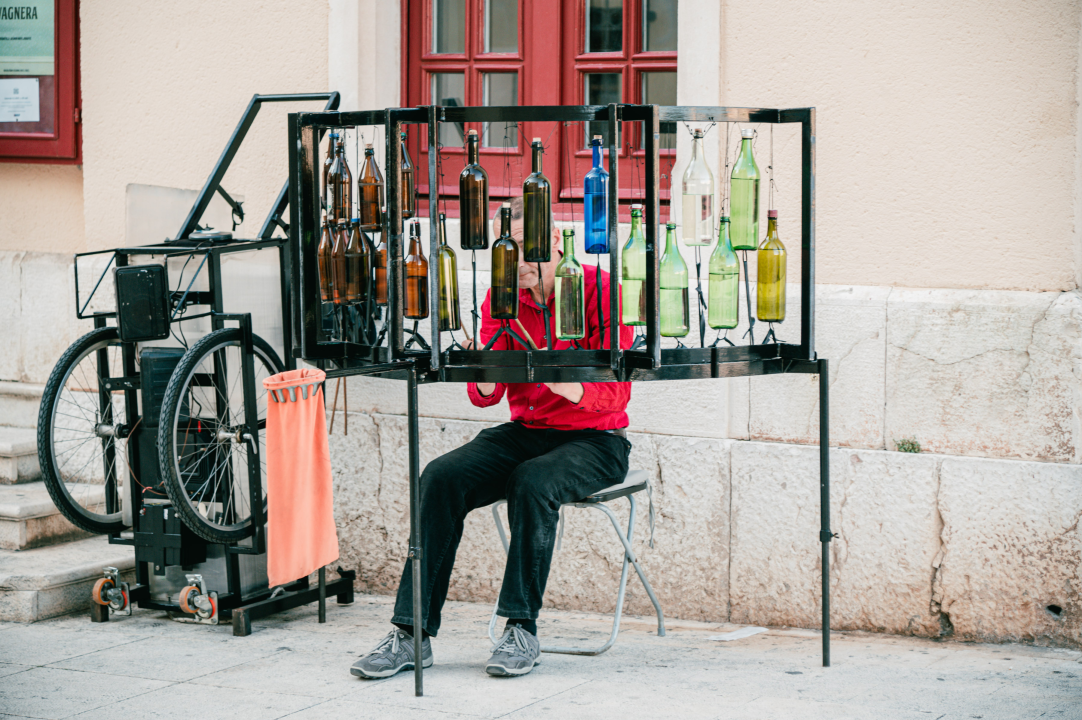 Ljetna atmosfera ispred kazališta uz uličnog svirača koji svira boce